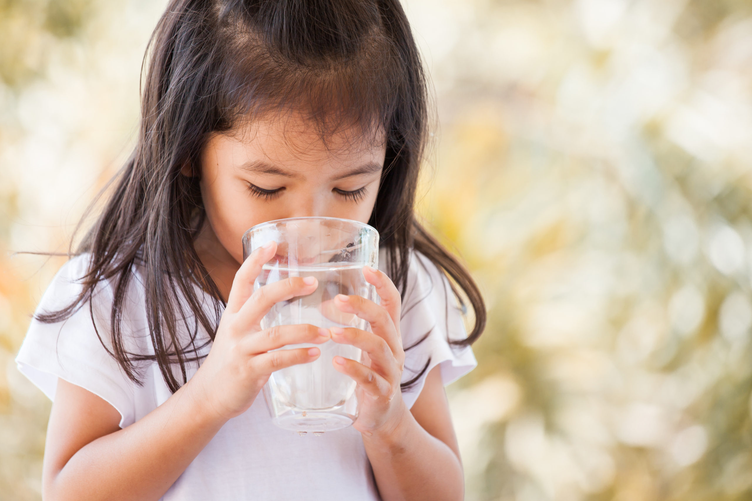 Cute asian little girl drinking fresh water from glass in vintage color tone